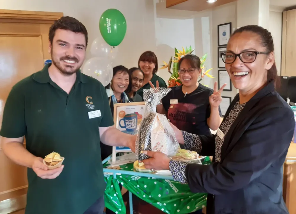 Sam Reid, Home Manager of The Aldbury, presents the Golden Cup Cake prize to winner and Housekeeping colleague Michael Sheppard. With them are, from second left: colleagues Merle Foster, Kanya Brannon, Janette Burgess and Nimpha Salmon